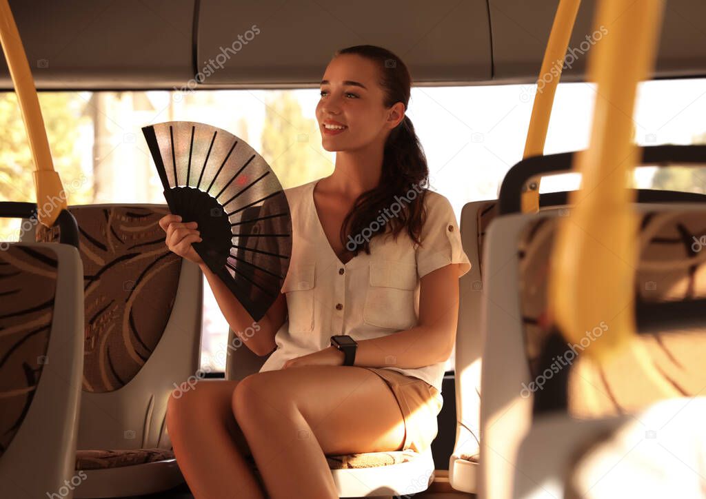 Young woman using hand fan in bus on hot summer day