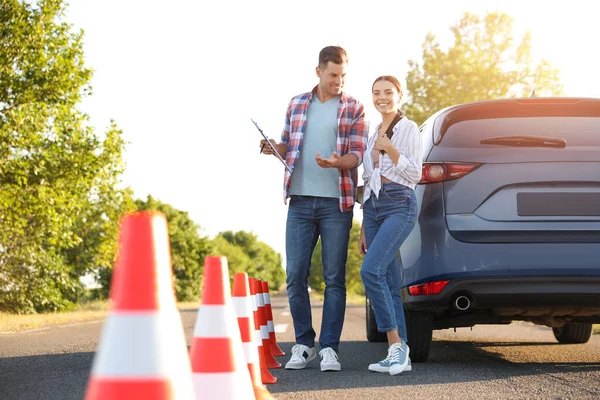 Instructor with clipboard and his student near car outdoors. Driving school exam