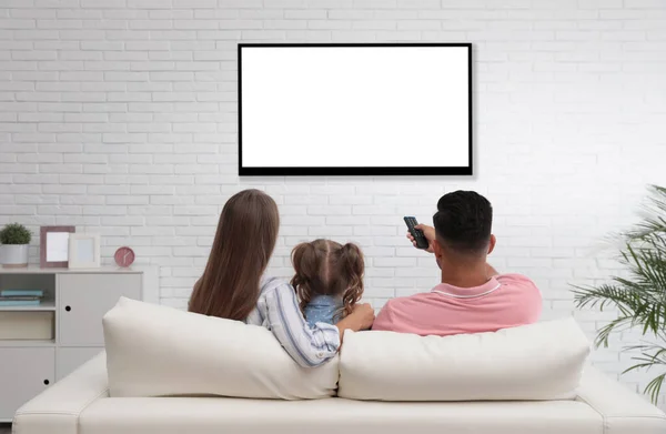 Family watching TV on sofa at home, back view