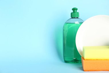 Temizlik ürünleri, süngerler ve açık mavi arka planda tabak, yazı için yer. Bulaşık malzemeleri.