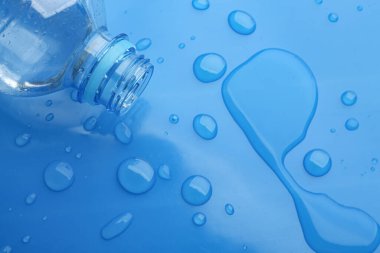 Mavi arka planda dökülen su damlaları ve plastik şişe, üst manzara