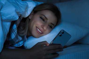 Genç bir kadın gece yatakta akıllı telefon kullanıyor. Nomofobi ve uyku bozukluğu sorunu