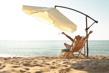 Kumsalda güverte sandalyesinde dinlenen bir adam. Yaz tatili