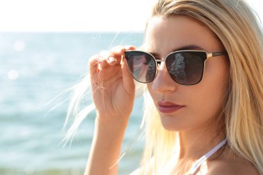 Güneşli bir günde deniz kenarında güneş gözlüğü takan güzel bir kadın.