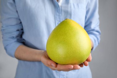 Açık gri arka planda taze bir çiçek tutan kadın, yakın plan.