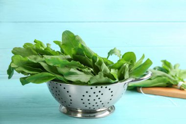 Açık mavi ahşap masada kevgir yapraklarıyla taze yeşil kuş yaprakları.