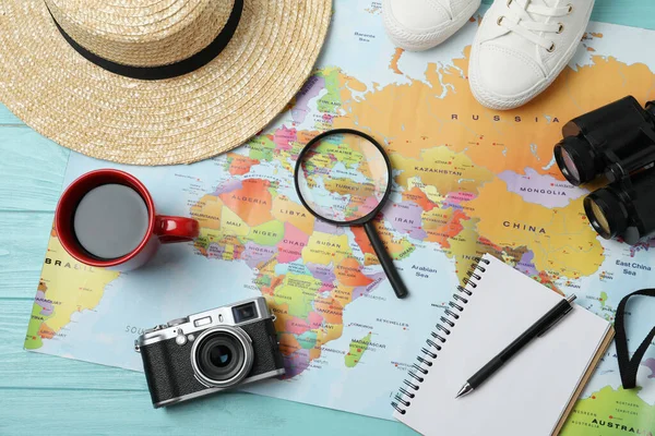 Flat lay composition with world map and different travel accessories on turquoise wooden table. Planning summer vacation trip