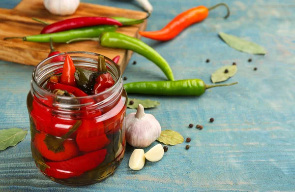 Glass jar of pickled chili peppers on light blue wooden table. Space for text