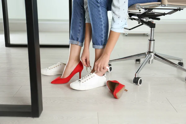 Woman taking off uncomfortable shoes and putting on sneakers in office, closeup. Tired feet after wearing high heels