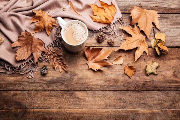 Düz kompozisyon, bir fincan sıcak içecek ve sonbahar yaprakları ile ahşap masa üzerinde, metin için boşluk. Sıcak atmosfer