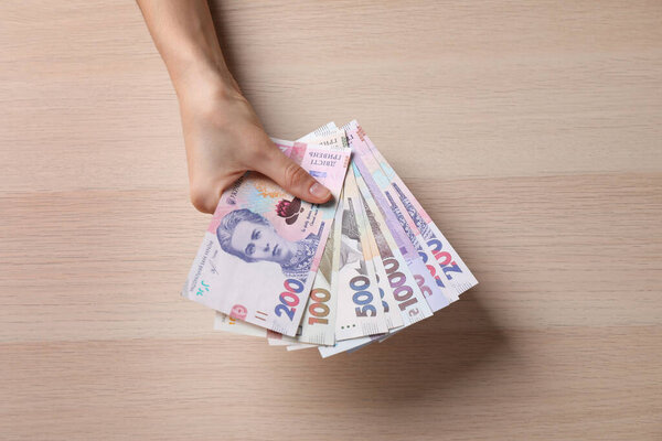 Woman holding Ukrainian money on wooden background, closeup