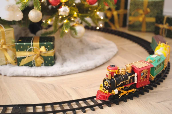 Toy train and railway near Christmas tree indoors. Space for text