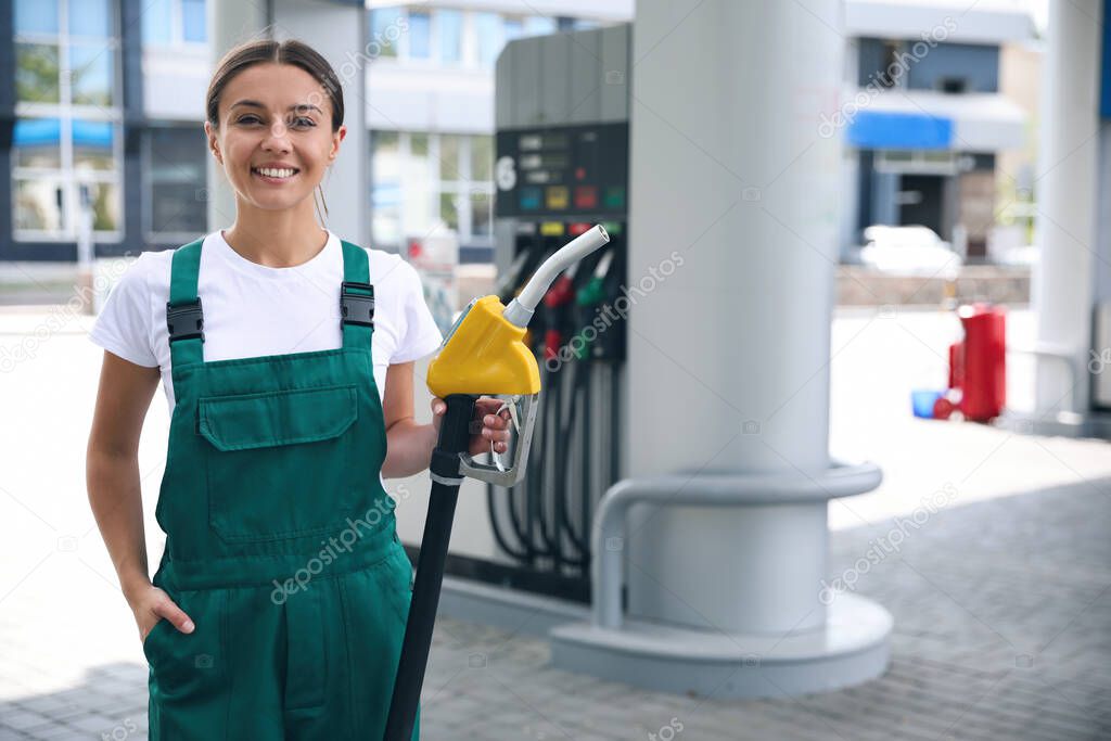 Young worker with fuel pump nozzle at modern gas station