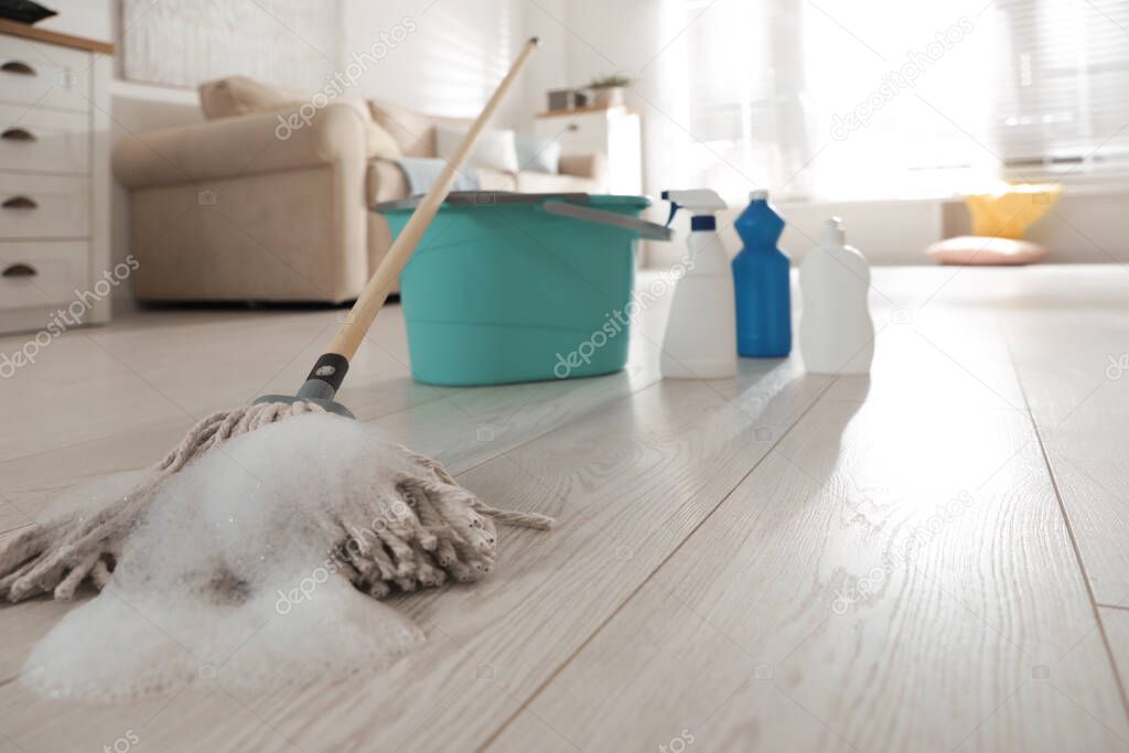 Bucket and different cleaning products indoors, focus on mop with foam
