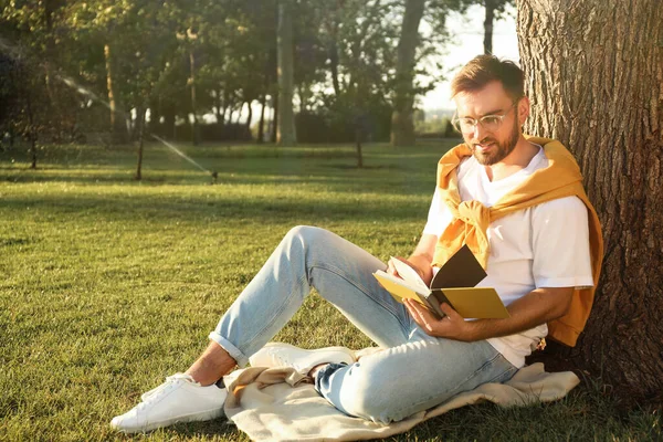 Молодой Человек Читает Книгу Зеленой Траве Возле Дерева Парке — стоковое фото