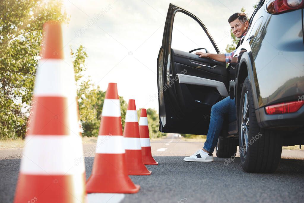 Man in car near traffic cones outdoors. Driving school exam