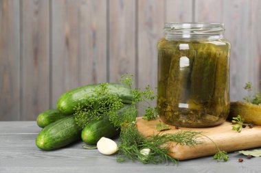 Cam kavanoz dolusu salatalık turşusu ve gri ahşap masa malzemeleri.