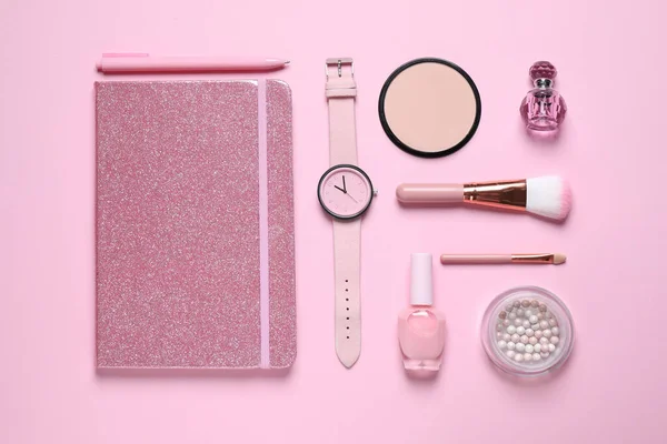 Flat lay composition with notebook, wristwatch and cosmetics on pink background