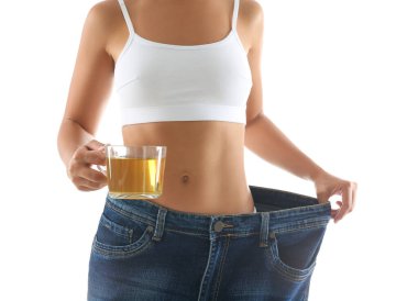 Yaşlı, büyük kotlu ve elinde çay bardağı olan genç bir kadın beyaz arka planda diyet sonuçlarını gösteriyor.