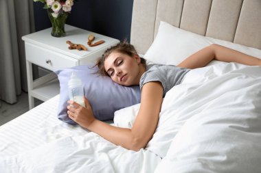 Bir şişe sütle evde uyuyan bitkin bir anne.