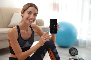 Genç kadın akıllı telefonu evde fitness uygulaması ile gösteriyor