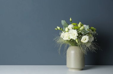 Üzerinde güzel Eustoma çiçekleri olan bir buket, gri arka planda, beyaz masadaki vazoda. Metin için boşluk