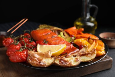 Lezzetli pişmiş somon ve sebzeler siyah masada servis ediliyor, yakın plan. Kızartmadan sağlıklı yemekler.