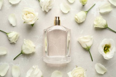 Açık gri mermer arka planda parfüm ve çiçeklerle dolu düz bir şişe kompozisyonu vardı.