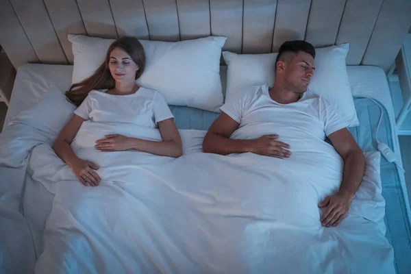 Couple sleeping on electric heating pad in bed at night, above view