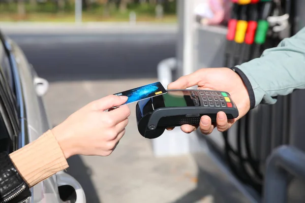 Woman sitting in car and paying with credit card at gas station, closeup