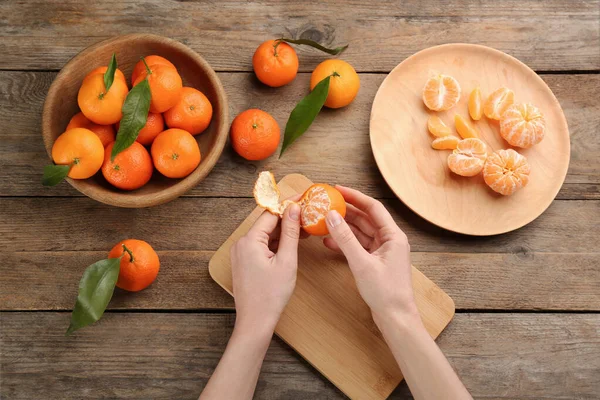 Woman peeling fresh ripe tangerine at wooden table, top view