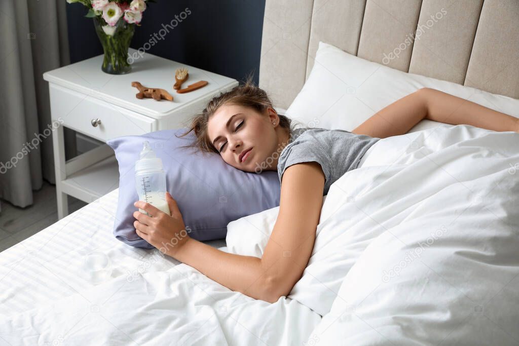 Exhausted young mother with bottle of milk sleeping in bed at home