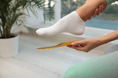 Woman fitting orthopedic insole indoors, closeup. Foot care clipart