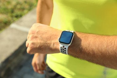 Man checking modern smart watch during training outdoors, closeup clipart