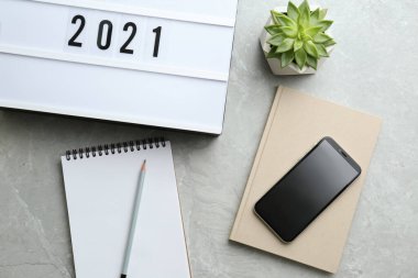 Defterlerin yanında 2021 numaralı ışık kutusu ve telefon gri masanın üstünde, düz yerde. Yeni yıl hedefleri