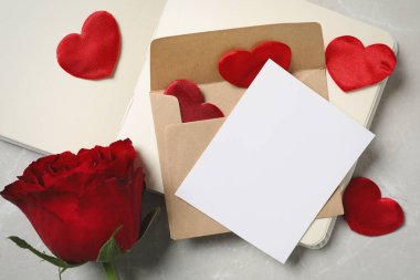 Üzerinde boş tebrik kartı olan kompozisyon, açık gri mermer masanın üzerinde gül ve defter var. Sevgililer Günü kutlaması