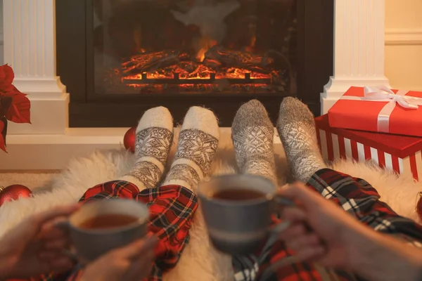Couple with hot drinks resting near fireplace at home, closeup