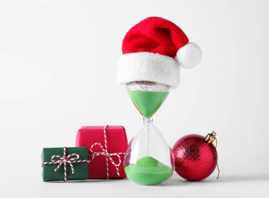 Noel Baba şapkalı kum saati ve beyaz arka planda şenlik dekoru. Noel geri sayımı