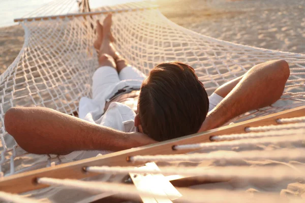 日落时在海滩上的吊床上休息的男人 — 图库照片