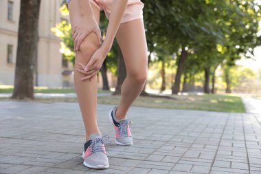 Şehir caddesinde diz sorunu olan genç bir kadın, yakın plan.