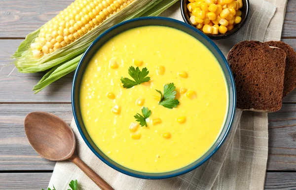 Delicious creamy corn soup served on wooden table, flat lay