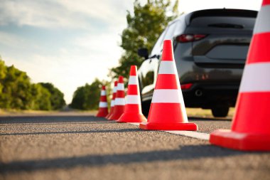 Açık havada arabanın yanında trafik konileri var. Ehliyet sınavı