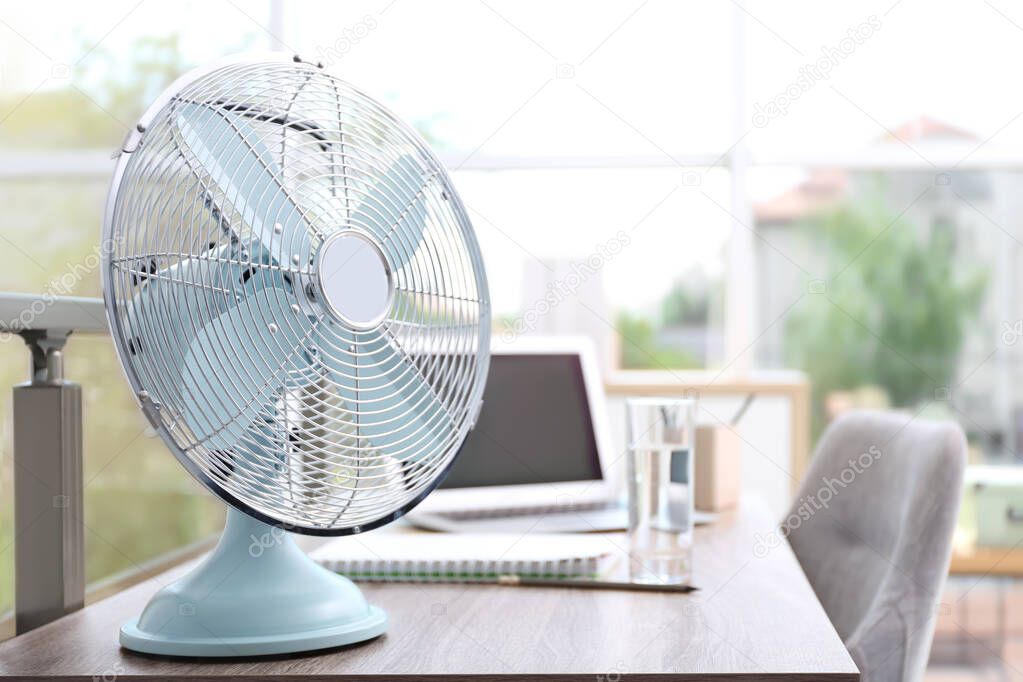 Modern fan on wooden table in office, space for text. Summer heat