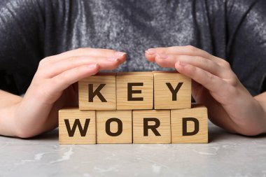 Gri mermer masada KEYWORD sözcüğüyle küpleri gösteren kadın, yakın plan.