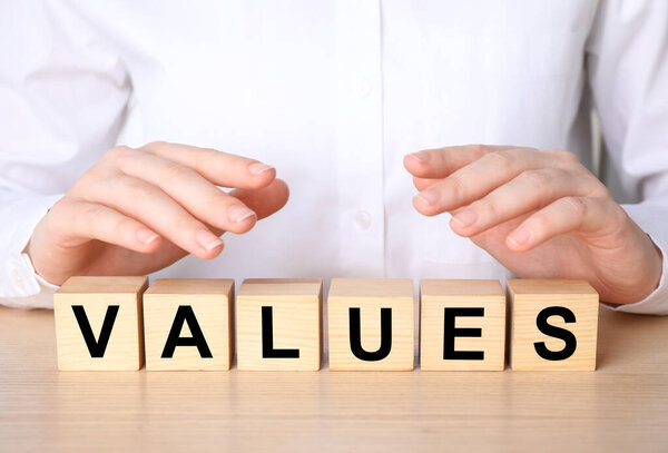 Core values concept. Woman with cubes at wooden table, closeup