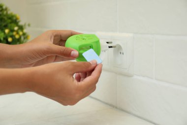 Kadın evdeki elektrikli sivrisinek cihazına böcek kovucu koyuyor, yakın plan.