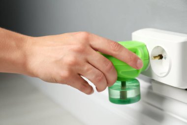 Kadın evinde böcek kovucu sıvıyla elektrik buharlaştırıcıyı fişe takıyor.