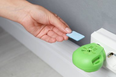 Kadın evdeki elektrikli sivrisinek cihazına böcek kovucu koyuyor, yakın plan.