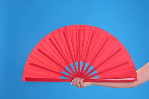 Woman holding red hand fan on light blue background, closeup