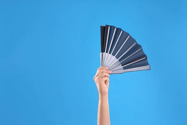 Woman holding black hand fan on light blue  background, closeup